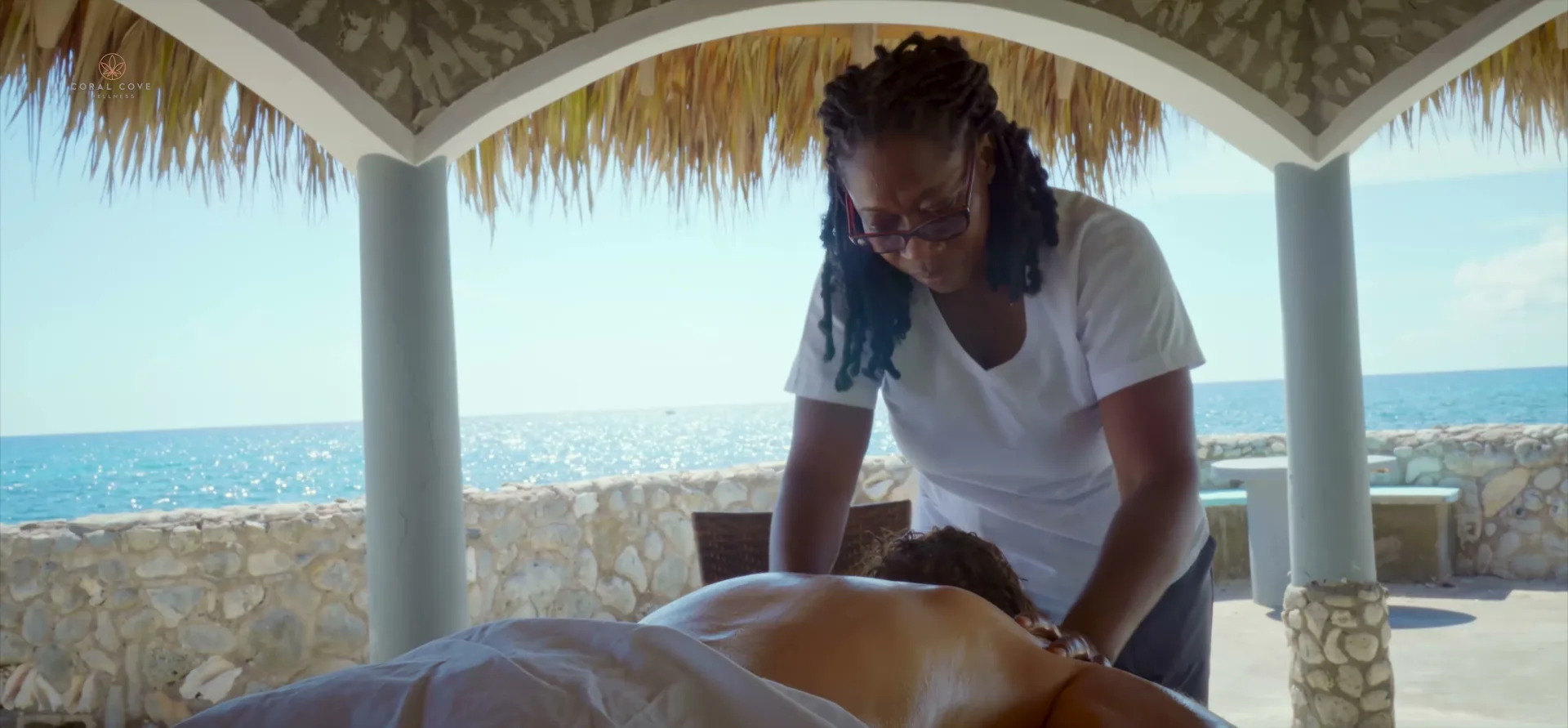 A guest receiving a massage in Coral Cove's open-air pavilion with the Caribbean Sea behind