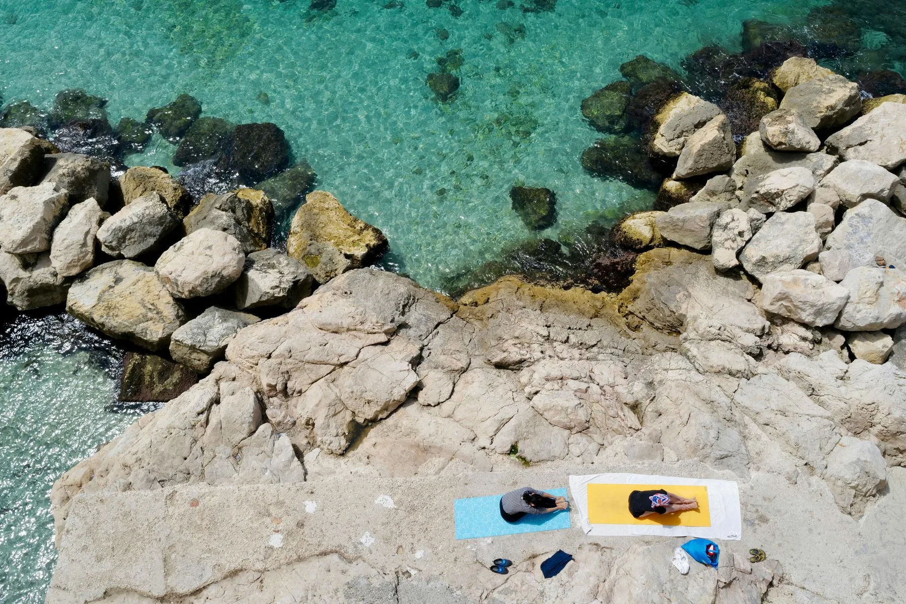 Yoga mats arranged on Coral Cove's rocky coast beside turquoise Caribbean water
